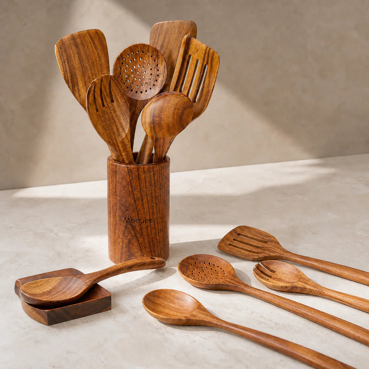 Mooues teak utensils with an engraved logo, arranged in a warm kitchen setting